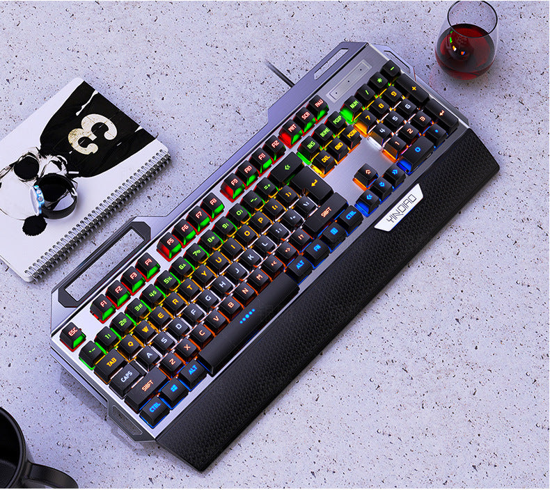 Mechanical keyboard with RGB lighting on a gray surface with a glass of red wine and notebook.
