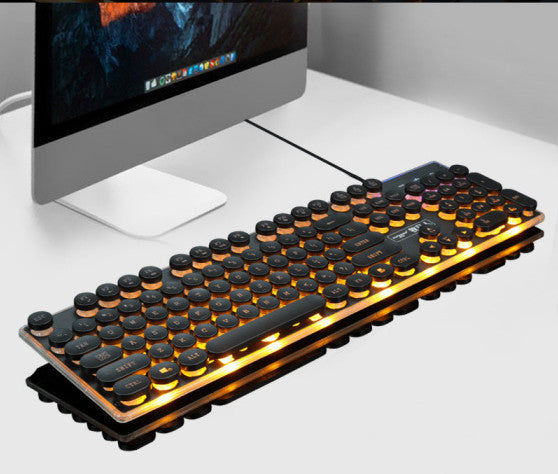 Mechanical keyboard with backlit keys in front of a computer monitor on a white desk.