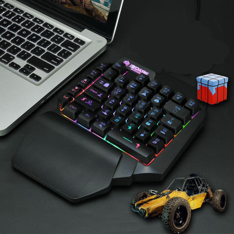 Gaming keyboard with colorful backlighting next to a laptop on a dark surface.