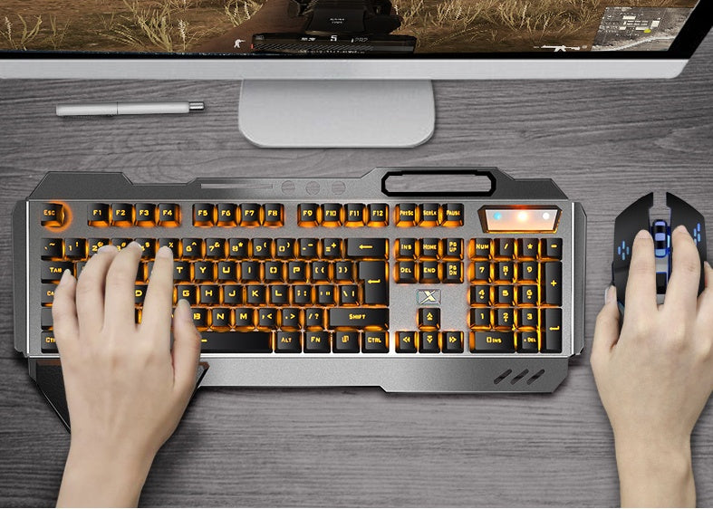 Person using a mechanical keyboard and mouse on a desk with a computer monitor in the background.