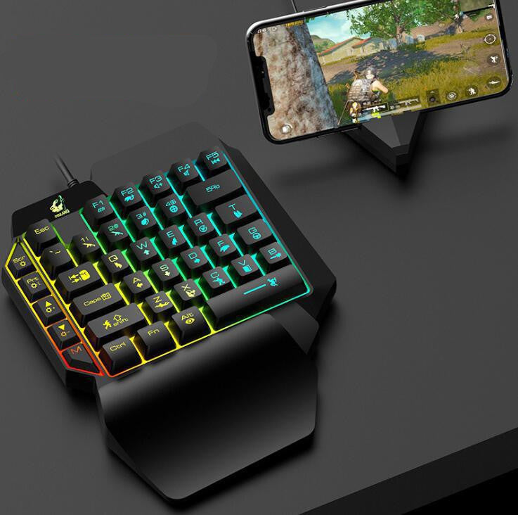 Gaming keyboard with RGB lighting on a dark surface, next to a smartphone displaying a game.