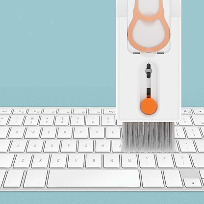 Keyboard cleaning brush with orange handle on a keyboard against a light blue background