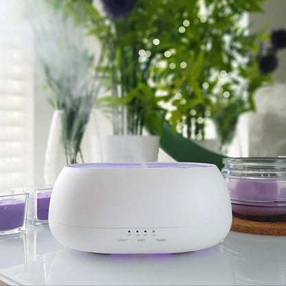 White diffuser with purple light on a table with plants and candles in the background