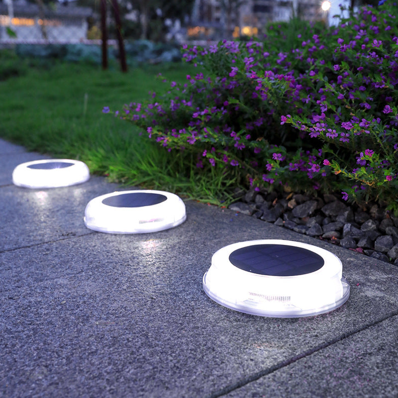 Solar-powered outdoor lights on a pavement next to a bush with purple flowers