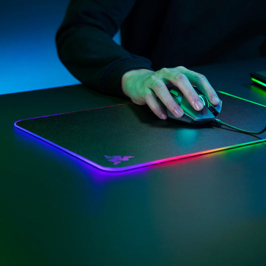 Hand using a mouse on a Razer mouse pad with colorful lighting effects.