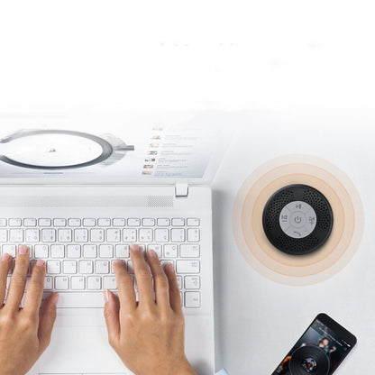 Person using a laptop with a wireless charging pad and speaker on a white surface