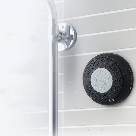 Black speaker in the shower with textured surface mounted on a tiled shower wall.