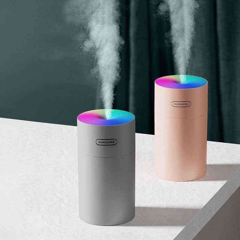 Two humidifiers, one gray and one pink, emitting steam on a white surface with a dark curtain background.