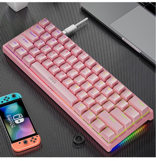 Pink keyboard with RGB lighting on a dark surface next to a smartphone and laptop.