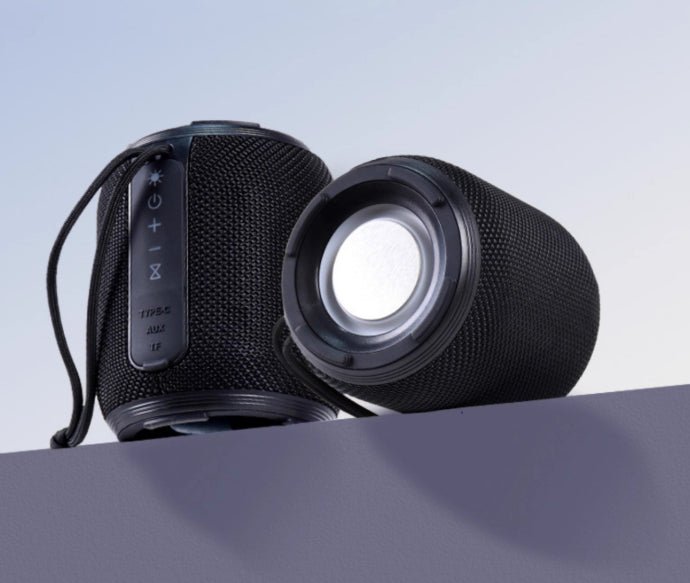 Black portable speaker on a light gray surface with a light blue background