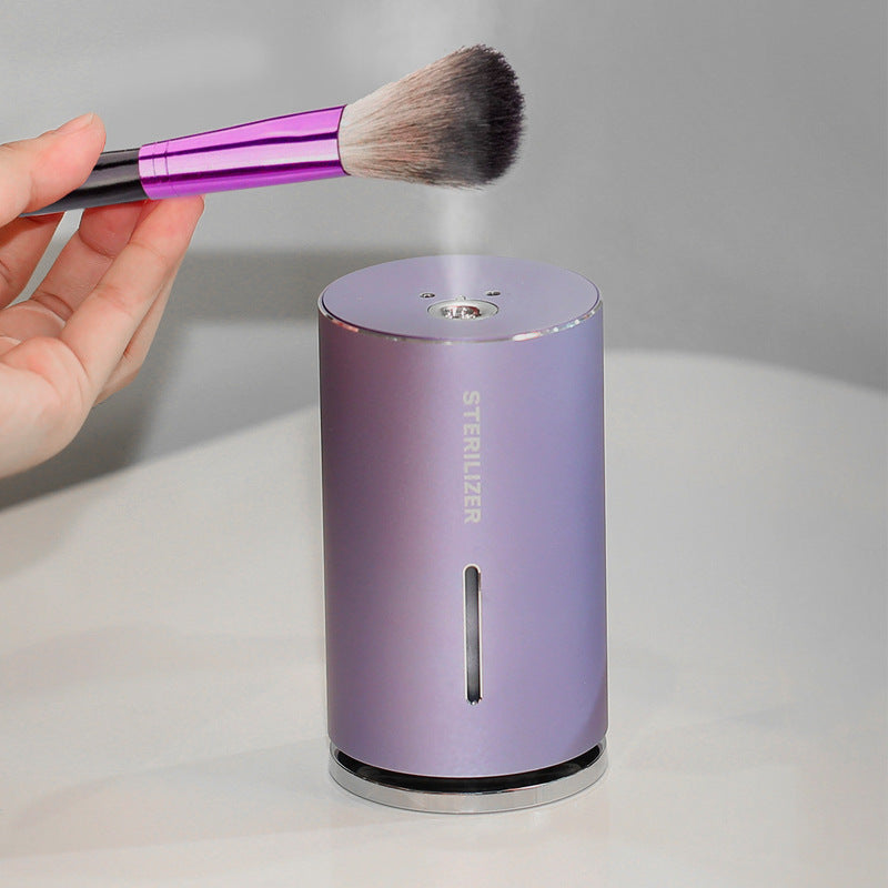 Purple sterilizer with a hand holding a makeup brush above it on a gray background