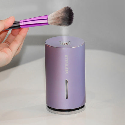 Purple sterilizer with a hand holding a makeup brush above it on a gray background
