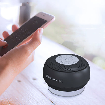 Black Bluetooth speaker with remote control on a light surface