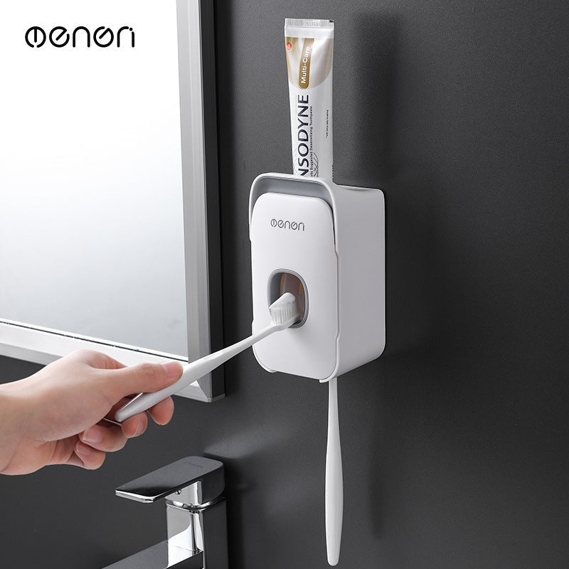 Hand using a toothbrush with a wall-mounted toothpaste dispenser labeled 'oenon' on a dark wall.