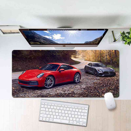Desk setup with a large mouse pad featuring two sports cars, a computer monitor, keyboard, and mouse.