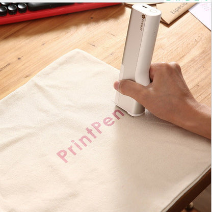 Hand using a white printing pen on a beige surface with 'PrintPen' branding.