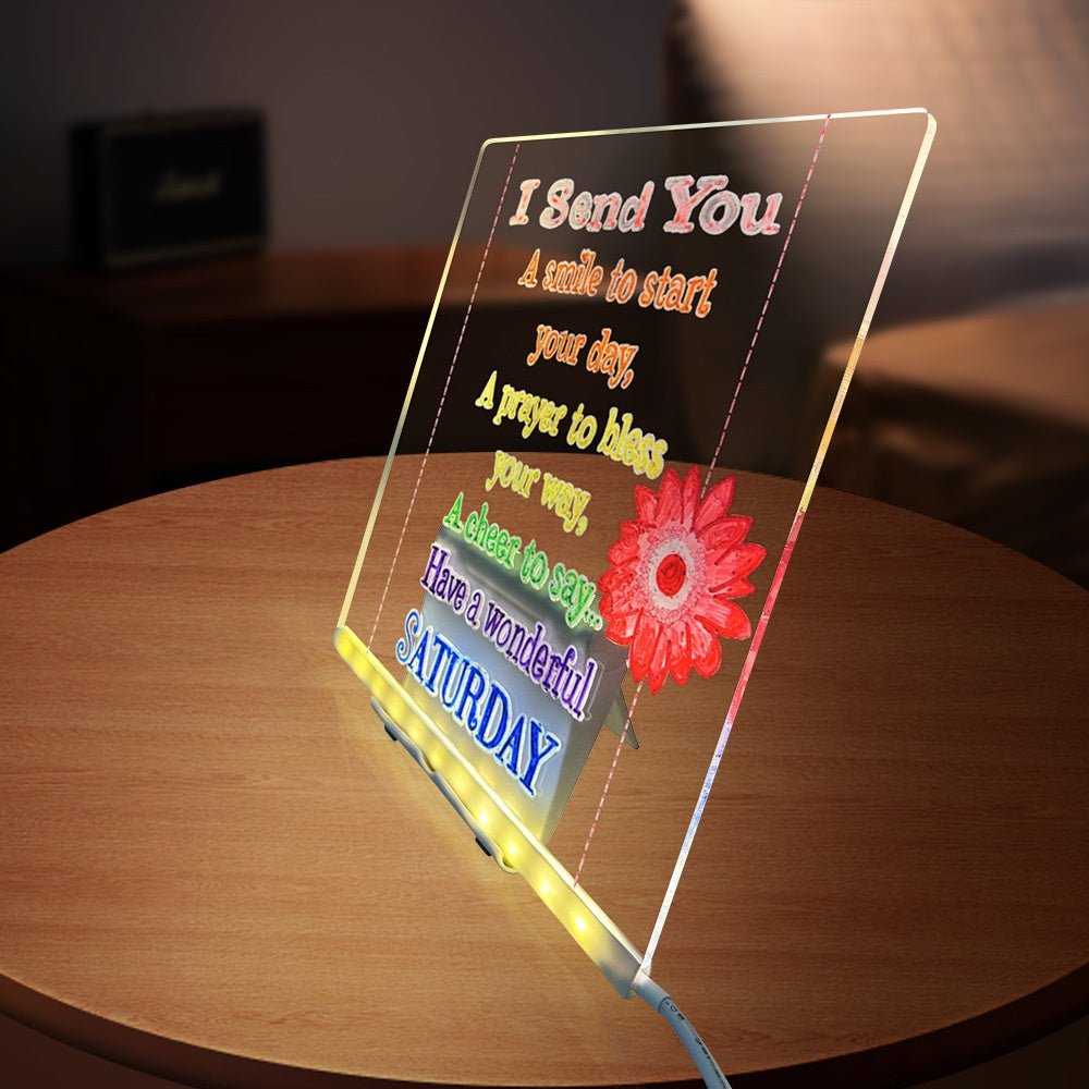Transparent LED sign with colorful text and a flower on a wooden surface