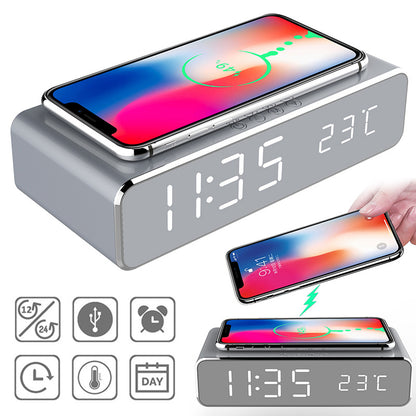 Gray digital clock with wireless charging pad and smartphone on top, displaying time and temperature.
