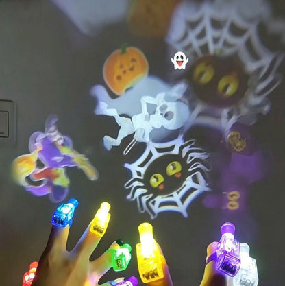 A hand holding multiple small LED nail light toys glowing in different colors, with colorful Halloween-themed projections on a dark wall including a spiderweb, jack-o'-lantern, ghost, and witch.