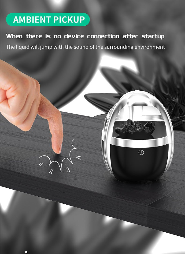 Black and silver device on a wooden surface with a hand pointing at it, surrounded by flowers.