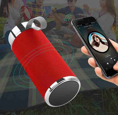 Red portable Bluetooth speaker with a phone displaying music app in an outdoor setting.