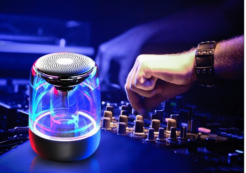 Colorful glowing cylindrical device on a DJ mixing console with a person's hand in the background.