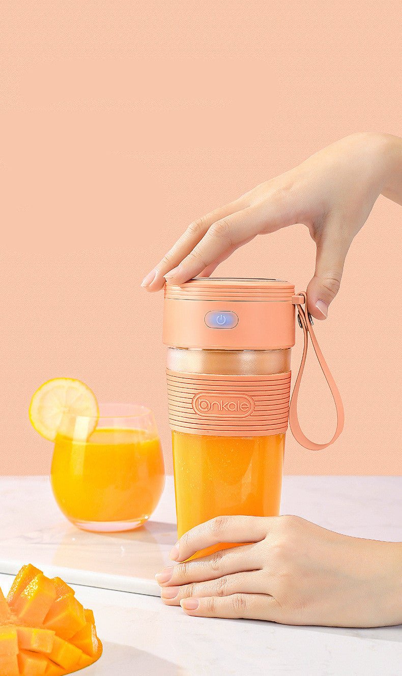 Person holding a pink and orange portable cup with a glass of orange juice and mango slices on a light background.