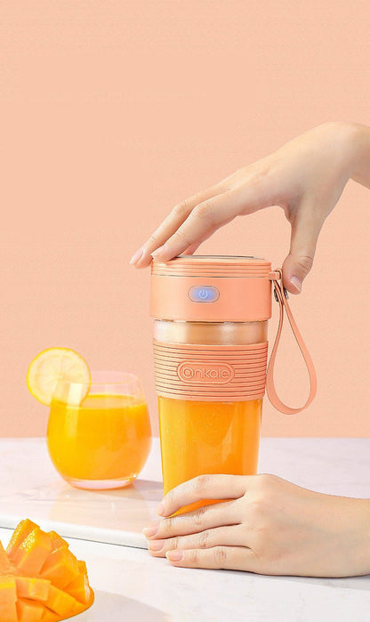 Person holding a pink and orange portable cup with a glass of orange juice and mango slices on a light background.