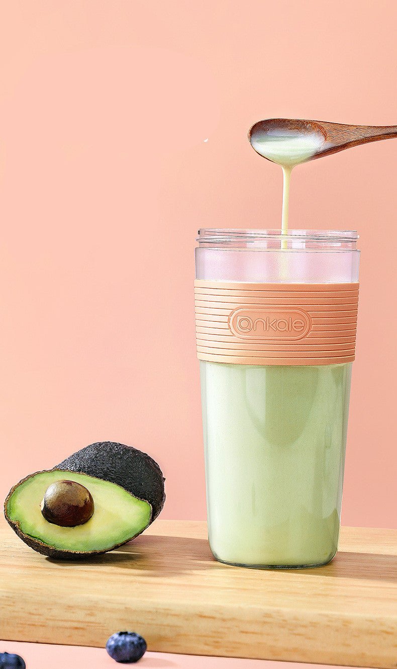 Avocado being mashed into a glass with a smoothie on a pink background