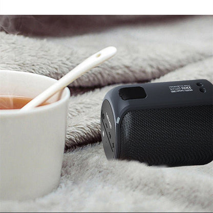 Black portable speaker on a soft surface next to a cup of tea and a toothbrush.