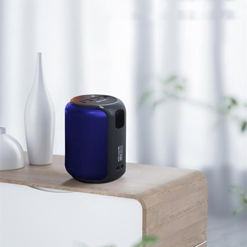 Blue and black portable speaker on a wooden surface with white vases and curtains in the background