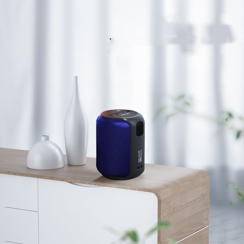 Blue and black portable speaker on a wooden surface with white vases and a blurred background