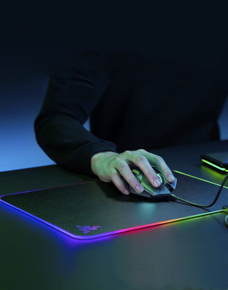 Person using a gaming mouse on a Razer mouse pad with RGB lighting.