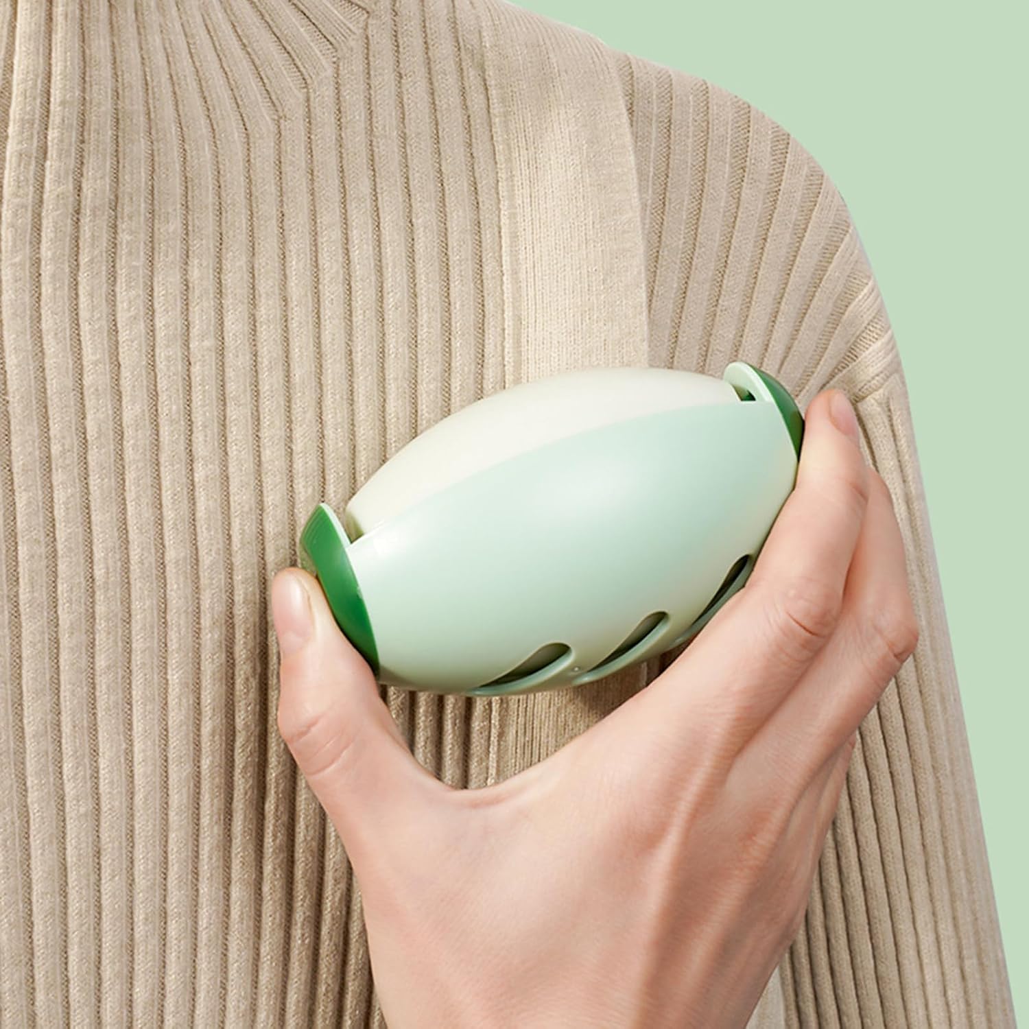 Hand holding a light green lint roller against a textured beige sweater