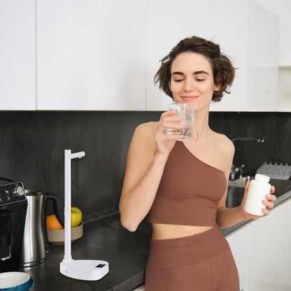 Woman in a kitchen holding a glass of water and a bottle, with a water filter in the foreground.