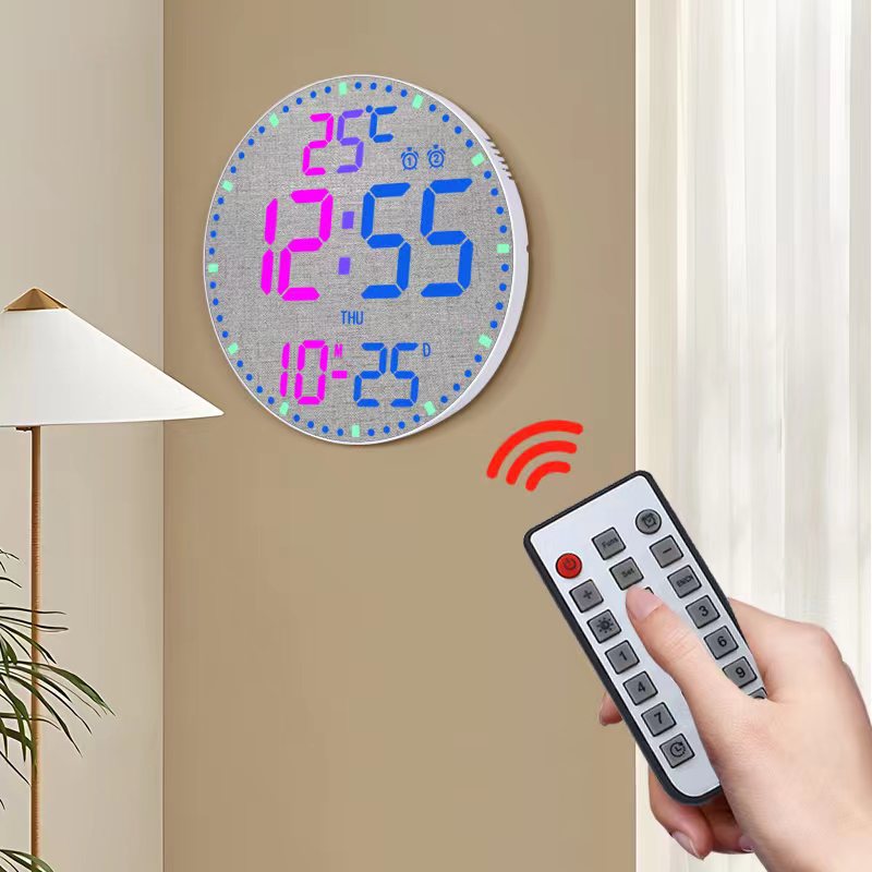 Digital wall clock with colorful display and remote control on a beige wall.