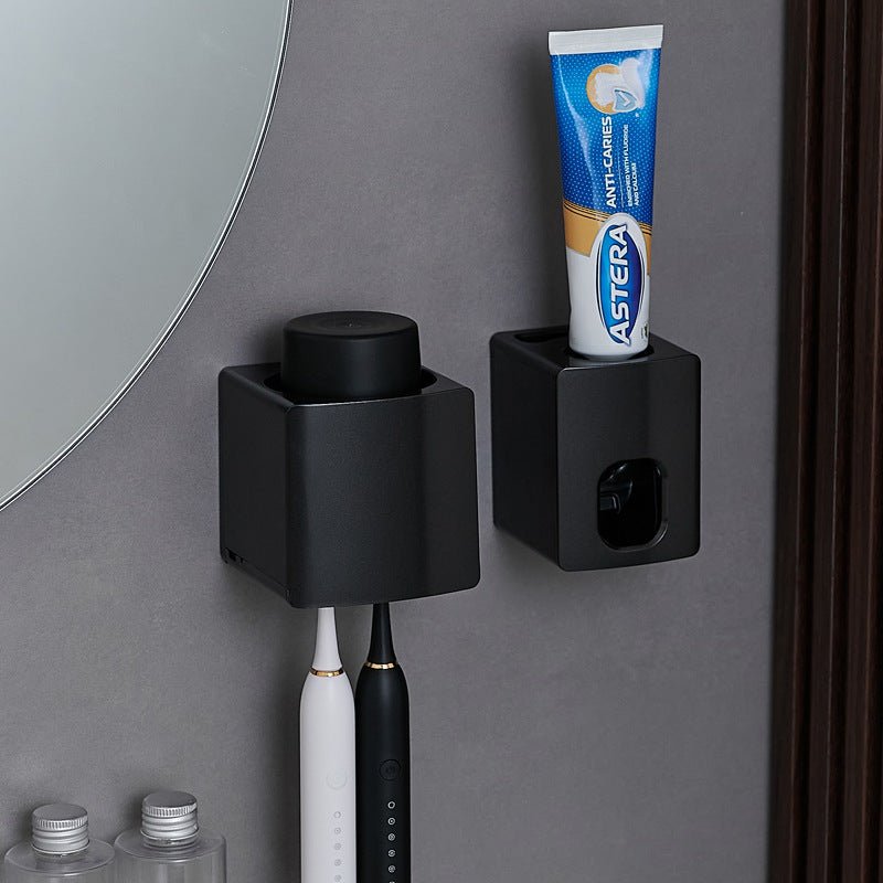Black wall-mounted toothbrush holder with a toothpaste tube on a gray bathroom wall.