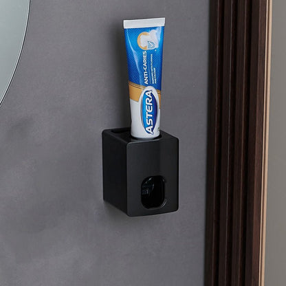 Black toothpaste holder with a tube of Astera toothpaste on a gray wall.
