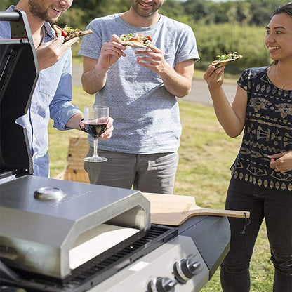 Three people enjoying pizza and wine near a portable grill outdoors.