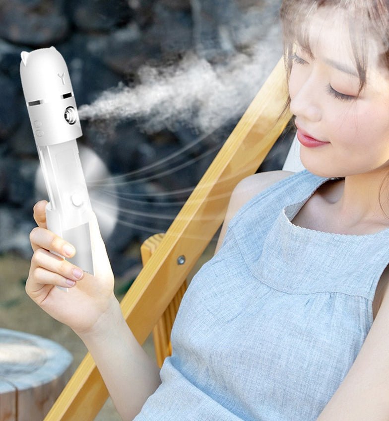 Woman using a handheld device emitting steam, possibly a nebulizer, with a blurred outdoor background.