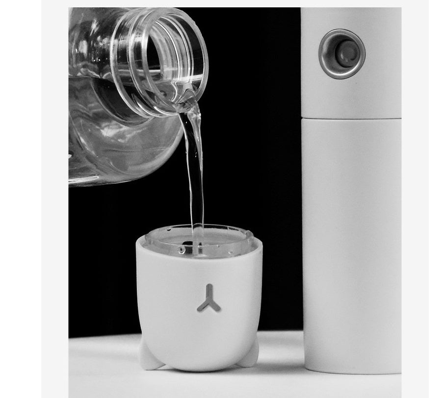 Clear liquid being poured into a white container with a logo, next to a white cylindrical device.