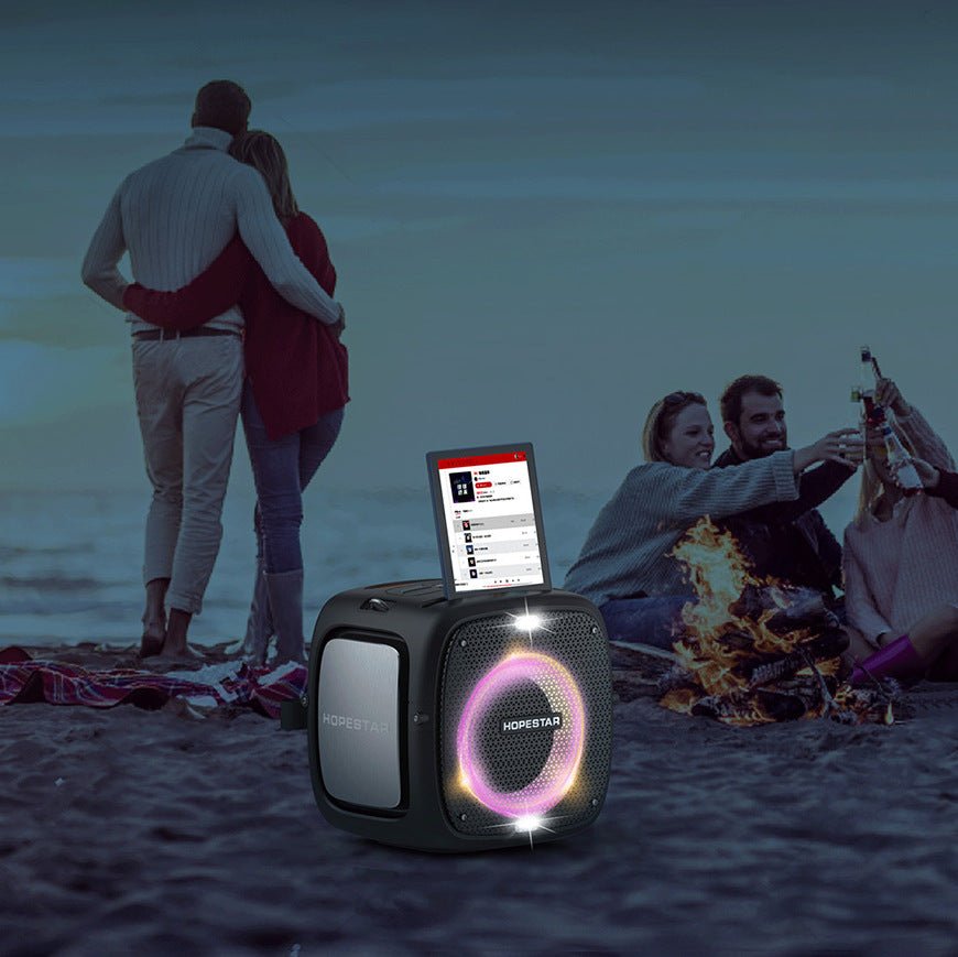 Portable speaker with screen on a beach at night, people around enjoying time together.