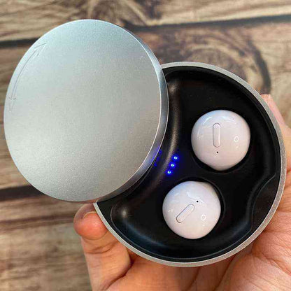 White wireless earbuds in a black charging case held by a hand on a wooden surface