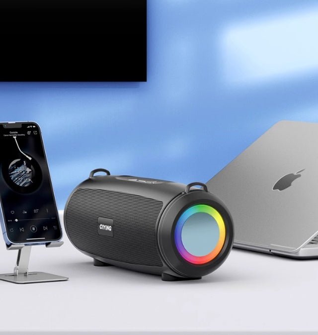 Black portable speaker with colorful LED lights next to a smartphone and laptop on a white surface.