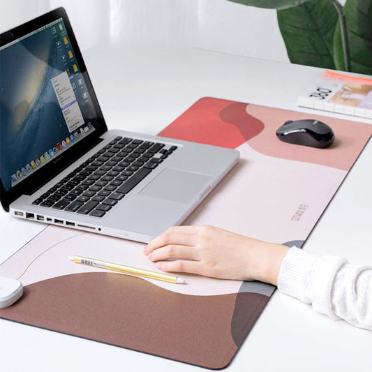 Laptop on a desk with a person's hand, mouse, and stationery items on a large mouse pad.
