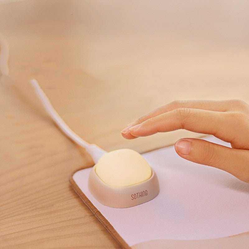 Hand interacting with a small round light on a desk, with 'SOTHING' branding visible.